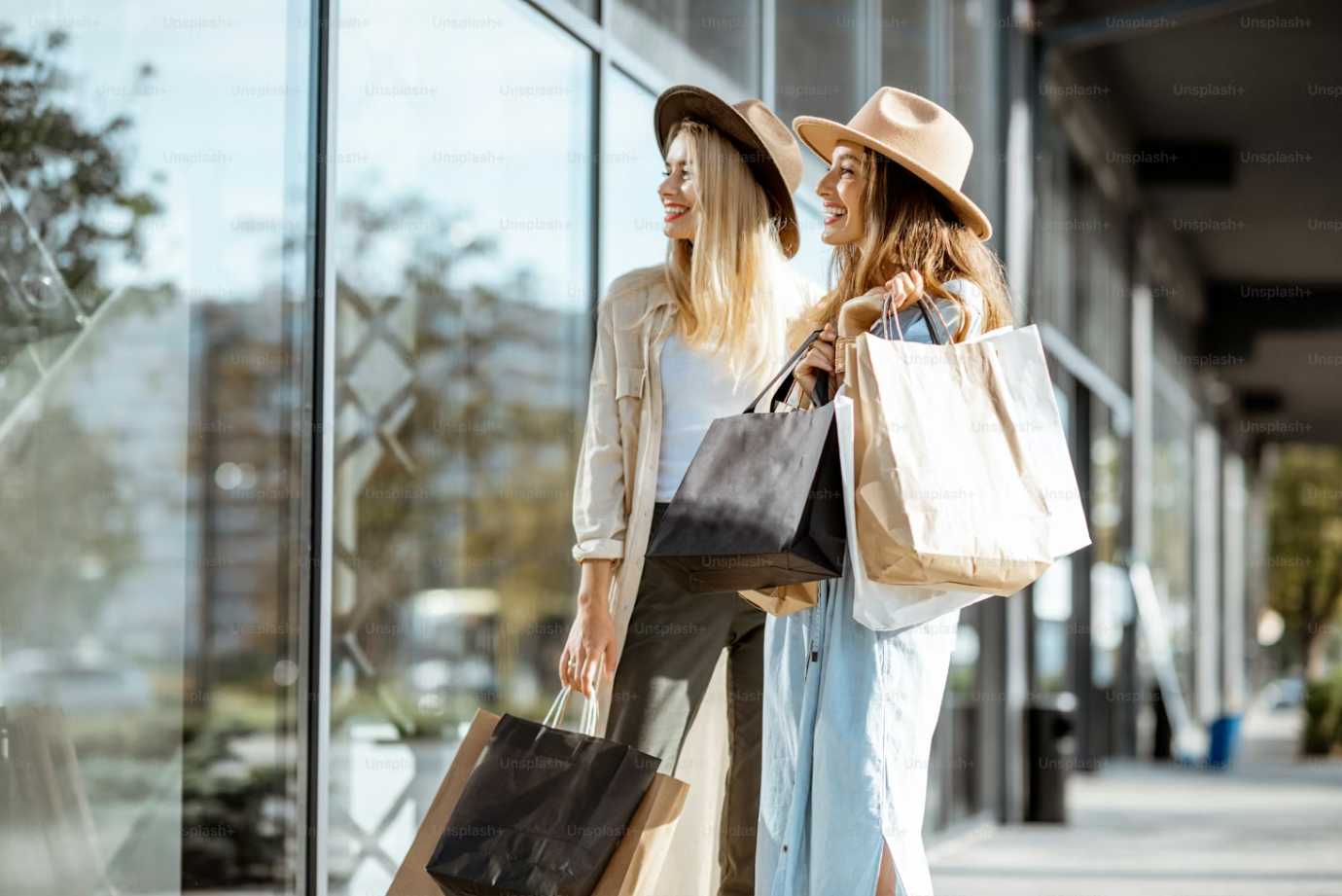 Two women with shopping bags walking past a store window.